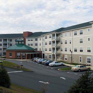 A view of a multi-story residential building with parking in front, set against a cloudy sky.