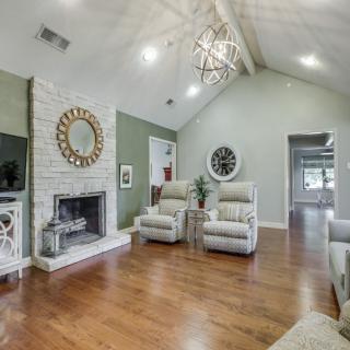 A spacious living room with a vaulted ceiling, featuring hardwood floors, a cozy fireplace, armchairs, and decorative mirrors.