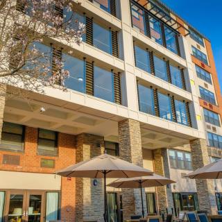 A modern multi-story building with large windows and outdoor seating under umbrellas.