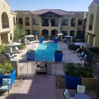 A view of an apartment complex with a central swimming pool surrounded by lounge chairs and umbrellas.