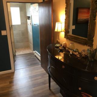A cozy hallway with wood flooring, featuring a stylish dresser and mirror, leading to a bathroom.