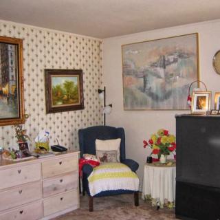 A cozy living room with vintage decor, featuring an armchair, artwork on the walls, a dresser, and a television.