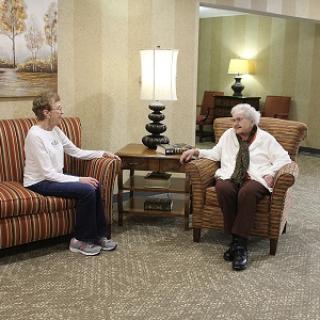 A caregiver and an elderly woman engaged in conversation in a cozy indoor setting.