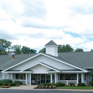 A white building with a gabled roof and landscaped surroundings against a cloudy sky.