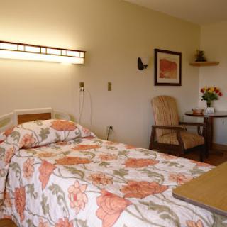 A cozy hospital room featuring floral bedding, a comfortable chair, and soft lighting.