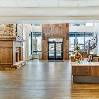 A spacious and modern lobby featuring a fireplace, wood paneling, and a reception desk with large windows providing ample natural light.