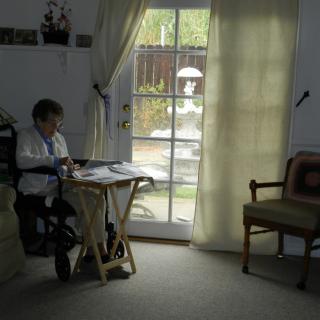 A person writing at a table near a window with curtains drawn, in a cozy room.