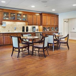 A modern kitchen and dining area featuring wooden cabinets, tables, and chairs on a hardwood floor.