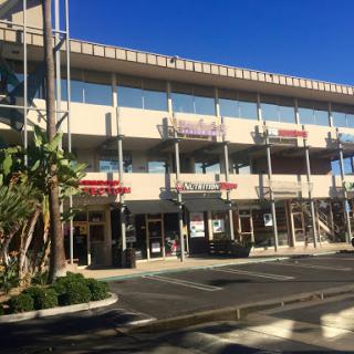 A sunny day at a retail shopping center featuring multiple storefronts and greenery.