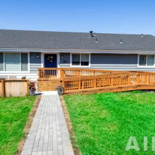 A single-story house with a wooden ramp and a well-maintained lawn under a clear blue sky.