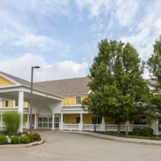 A yellow residential building with a covered entrance, surrounded by trees on a sunny day.