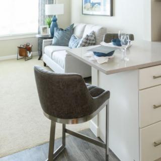 A modern living room with a sofa, decorative cushions, and a high chair next to a countertop.