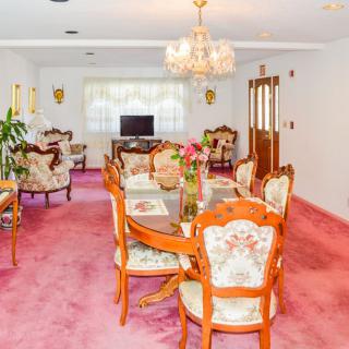 A vintage-style dining room with a pink carpet, elegant chandelier, and floral upholstered furniture.