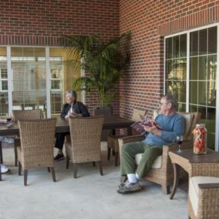 A group of people relaxing on a patio with wicker furniture and a brick wall backdrop.