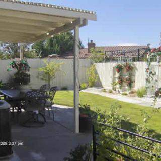 A sunny backyard with a covered patio and outdoor seating area overlooking a well-maintained garden and lawn.