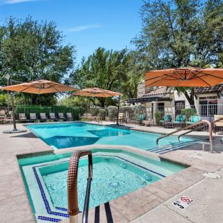 An inviting outdoor swimming pool area with a hot tub, surrounded by lounge chairs and sun umbrellas.