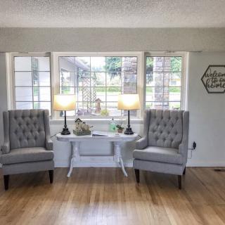 A cozy living room setup with two armchairs, a table, and lamps by a large window.
