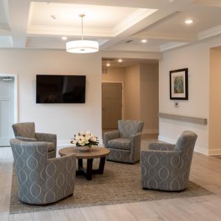 A modern living room with four patterned chairs around a round table, a mounted television, and ceiling lights.