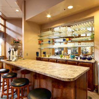 A cozy bar setup with a marble countertop and wooden stools, featuring mirrored shelves stocked with bottles.