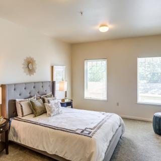 A modern bedroom with a neatly made bed, stylish decor, and ample natural light from two windows.