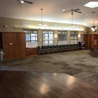 A spacious community center room with chairs lined up against the wall, ceiling fans, and bright overhead lighting.