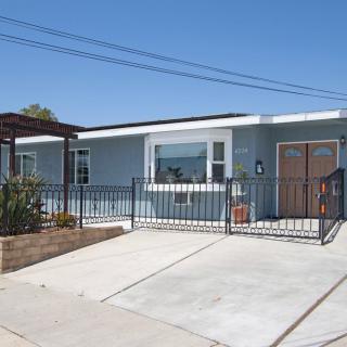 A single-story residential house with a driveway and fenced front yard.