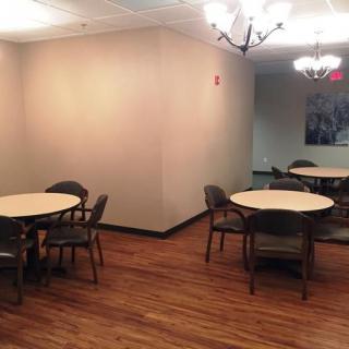 A cozy indoor dining area with wooden floors and several round tables surrounded by chairs.