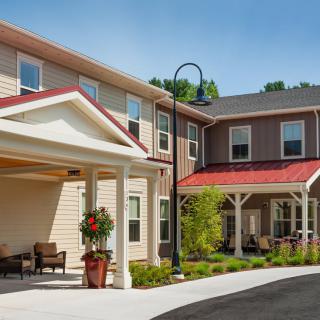 A modern residential building with a covered porch and well-maintained landscaping, photographed on a clear day.