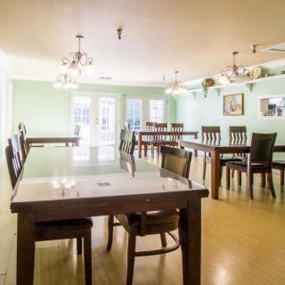 A spacious dining room with multiple tables and chairs, featuring elegant chandeliers and a wooden floor.