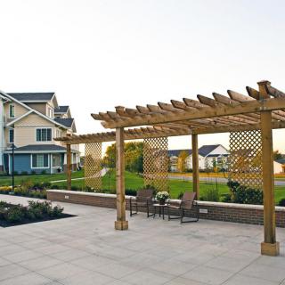 A suburban backyard with a wooden pergola and patio area, featuring outdoor seating amidst landscaped gardens.