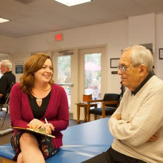 A woman and an elderly man having a friendly conversation indoors.