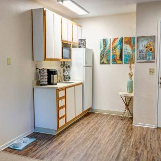 A modern kitchen with wooden flooring, white cabinets, and colorful artwork on the wall.