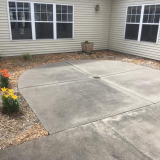 A concrete patio area with surrounding flower beds and windows on a building exterior.