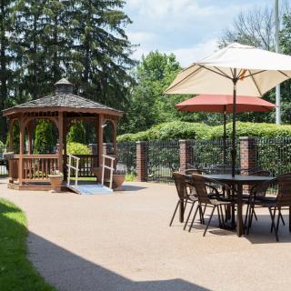 A tranquil outdoor patio featuring a wooden gazebo and seating area with umbrellas, surrounded by lush greenery.