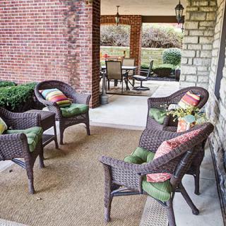 A cozy outdoor patio with wicker chairs and colorful cushions, set against a brick and stone backdrop.