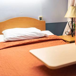A cozy bedroom setup with a neatly made bed featuring an orange blanket, a white pillow, and a table lamp beside it.
