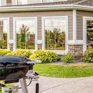 A backyard with a barbecue grill in front of a house featuring large windows.