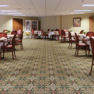 An elegant dining area featuring tables set with white tablecloths and comfortable chairs, adorned with a patterned carpet.