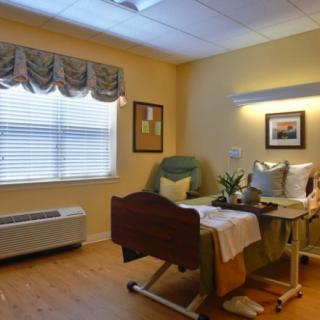 A well-furnished hospital room with a patient bed and comfortable seating, featuring a large window and wall decor.