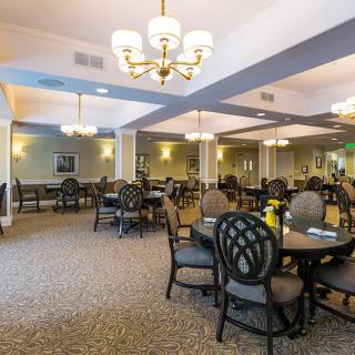 A spacious dining room with elegant chandeliers and neatly arranged tables and chairs.