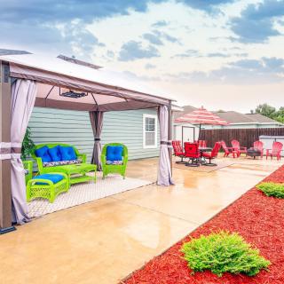A vibrant backyard patio featuring a gazebo with colorful seating and landscaped surroundings.