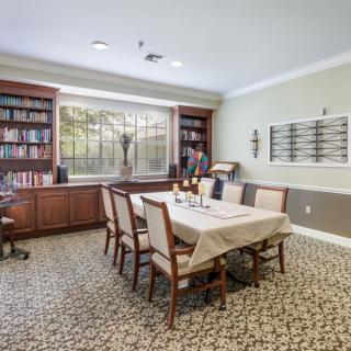 A cozy dining room with a table set for six, surrounded by bookshelves and a large window.