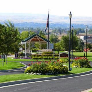 A scenic park with a gazebo, vibrant flower beds, and a flagpole.