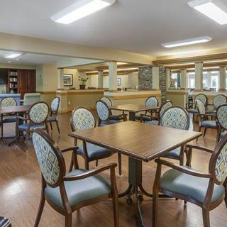 A spacious dining area with multiple tables and chairs, featuring a warm interior design and wooden flooring.