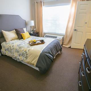 A cozy bedroom with a neatly made bed, soft pillows, and gentle lighting from a large window.