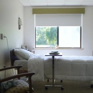 Empty hospital room with a neatly made bed and a view of greenery through the window.