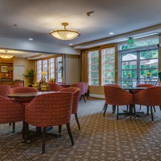 A cozy dining area with round tables, comfortable chairs, and large windows offering natural light.