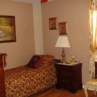 A cozy bedroom with a single bed, side table, and decorative paintings on the wall.