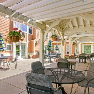 An outdoor patio with seating under a pergola, featuring hanging plants and tables with chairs.