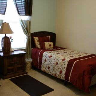 A cozy small bedroom with a single bed, nightstand, and window curtains.